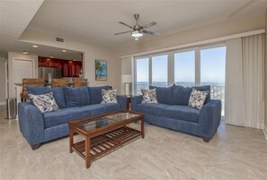A spacious living room with two blue sofas, a wooden coffee table, and a ceiling fan.