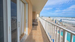 A balcony with a view of the ocean, a pool area with lounge chairs, and a door with a glass panel.