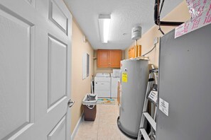A narrow hallway with a laundry area, including a washer and dryer, a refrigerator, and a trash can.
