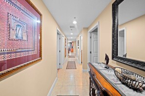 A hallway with a patterned wall, a wooden bench with a basket, and a large mirror.