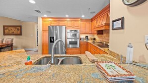 A kitchen with granite countertops, stainless steel appliances, wooden cabinets, and a clock on the wall.