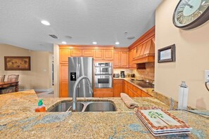 A kitchen with granite countertops, stainless steel appliances, wooden cabinets, and a clock on the wall.