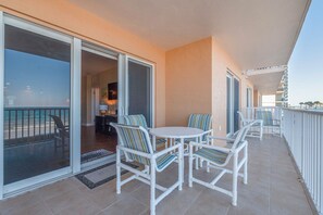 Un balcon avec des chaises blanches et une table, une porte-fenêtre coulissante donnant sur une pièce, et une vue sur l’océan.
