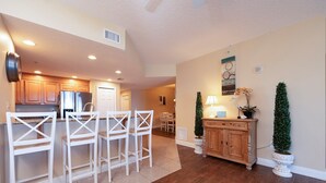 A modern kitchen with white bar stools, wooden cabinets, and a central island. - Gorgeous 3/3 Direct Oceanfront First Floor at the Sanibel Condominium Unit #104 (Daytona Beach Shores)