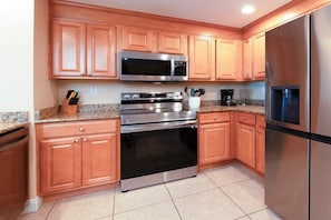Una cocina con armarios de madera, electrodomésticos de acero inoxidable, incluyendo un microondas, horno y refrigerador, y encimeras de granito.