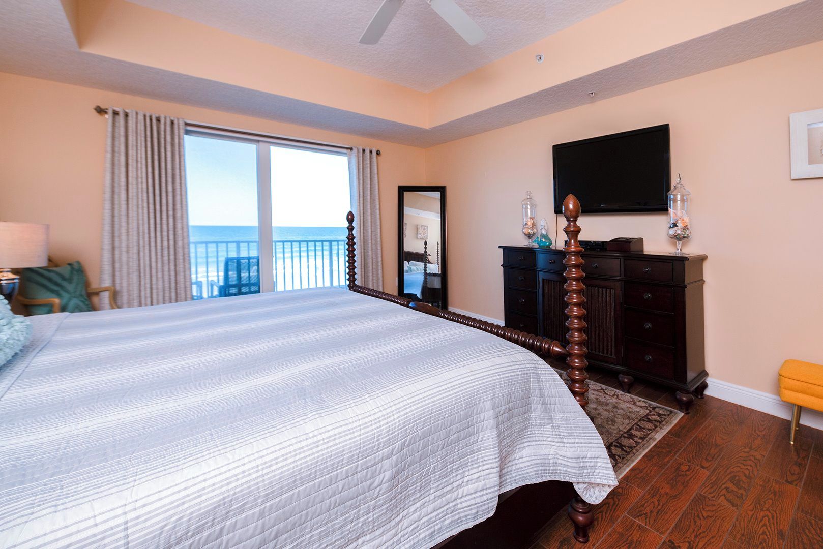 A bedroom with a large bed, a dresser, a television, and a view of the ocean.