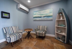 Una habitación con dos sillones a rayas, una pequeña mesa redonda, un cuadro de una vista marina y un estante decorativo con un pez y un cangrejo.