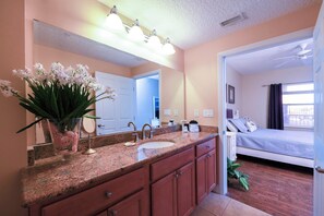 Une salle de bain avec un comptoir en granit, un lavabo, un miroir et un vase rempli de fleurs blanches.