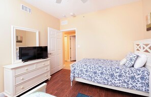 Un dormitorio con cama, cómoda, televisor y puerta que da a otra habitación.