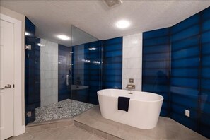 A modern bathroom with a glass-enclosed shower, a freestanding bathtub, and blue-tiled walls. - Penthouse #1102 - Direct Oceanfront NE Corner  Luxury 3/3  Sanibel Condominium (Daytona Beach Shores)