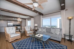 A spacious living room with a large window, a ceiling fan, and a view of the city.