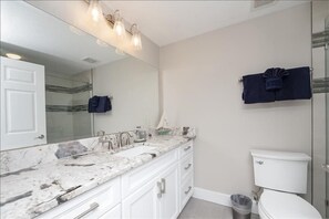 A bathroom with a marble countertop, a white toilet, and a glass shower enclosure.
