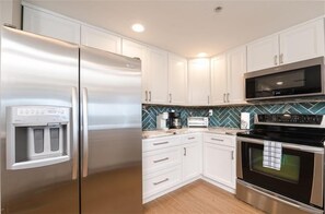 A modern kitchen with white cabinets, a stainless steel refrigerator, a microwave, and an oven.