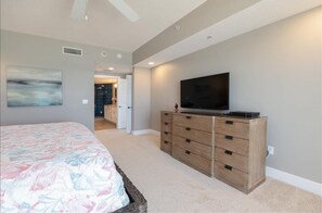 A bedroom with a bed, a dresser, a television, and a door leading to another room.