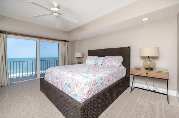 A bedroom with a large bed, a nightstand, a lamp, and a ceiling fan.