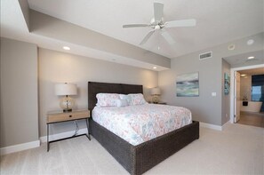 A bedroom with a bed, bedside lamps, a ceiling fan, and a painting on the wall.