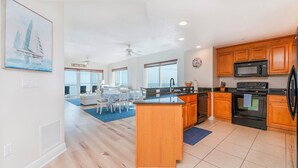 A modern kitchen with wooden cabinets, a central island, and a dining area with a view.