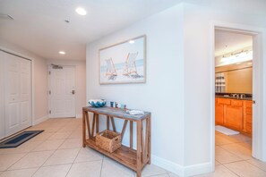 A hallway with a console table, a framed painting, and a view into a kitchen. - #705 Sanibel Direct Oceanfront SE Corner Unit 3/3 (Daytona Beach Shores)