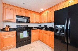 A kitchen with wooden cabinets, a black refrigerator, a microwave, a stove, and a coffee maker.