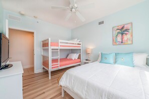 A bedroom with a bunk bed, a single bed, a desk with a computer, and a ceiling fan. - Stunning Ocean Views at 705 Sanibel (Daytona Beach Shores)