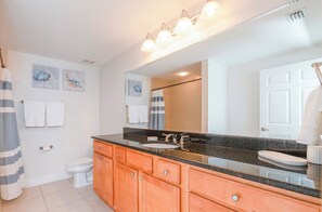 A bathroom with a large mirror, a sink, and a toilet. There are towels hanging on the wall and a shower curtain. - Stunning Ocean Views at 705 Sanibel (Daytona Beach Shores)