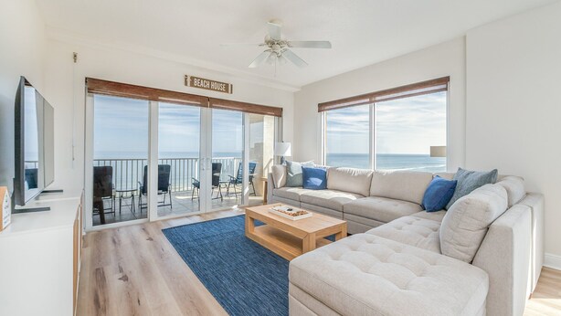 A spacious living room with a large sofa, a coffee table, and a view of the ocean through large windows.