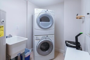 A laundry room with two stacked front-loading washing machines, a sink, and a trash bin. - #705 Sanibel Direct Oceanfront SE Corner Unit 3/3 (Daytona Beach Shores)