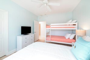Een slaapkamer met stapelbedden, een televisie op een dressoir en een plafondventilator.