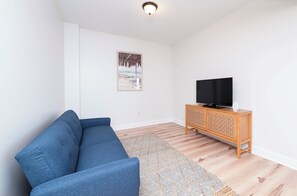 A living room with a blue sofa, a wooden cabinet with a TV, and a patterned rug.