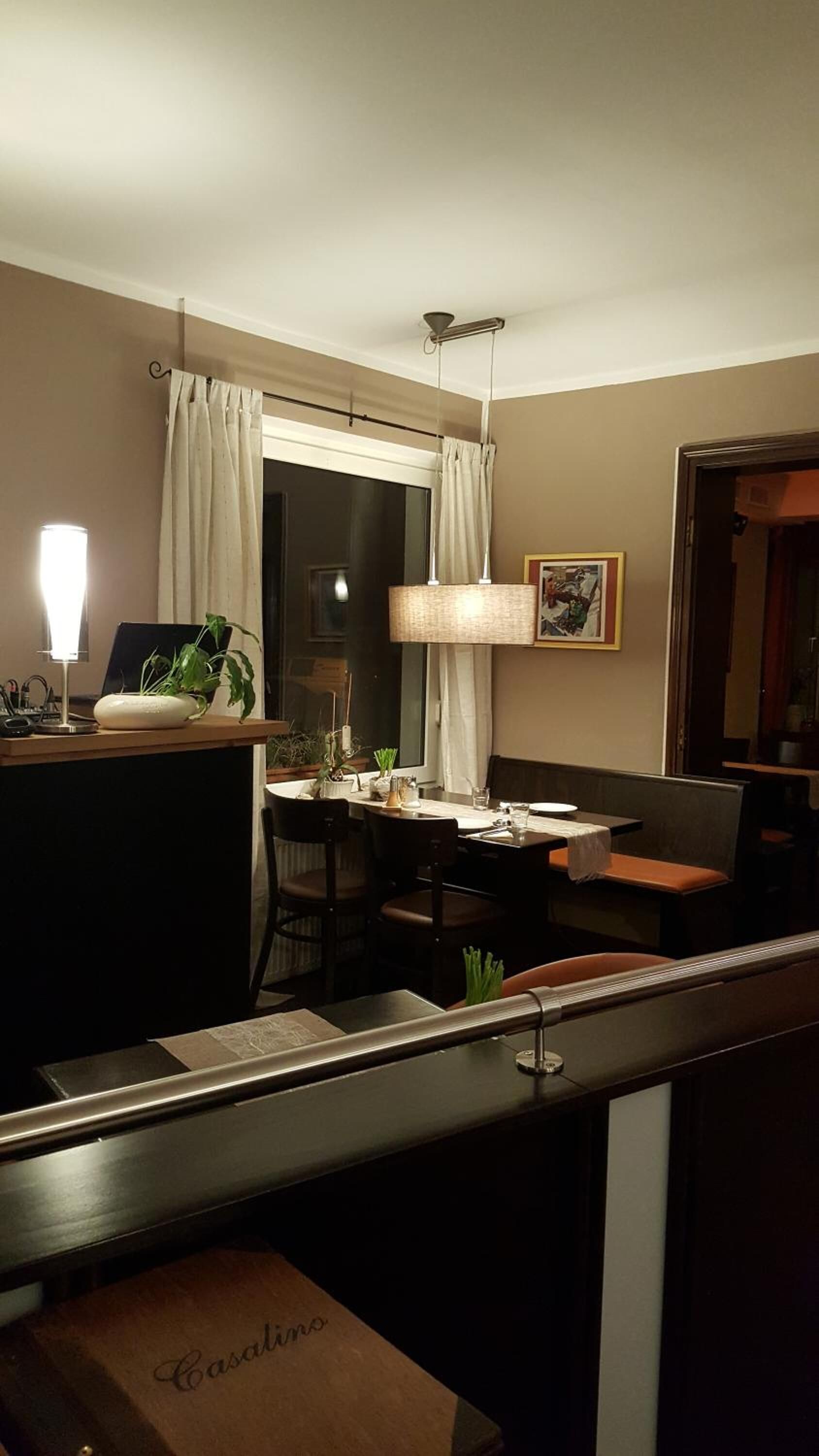 A hotel room with a dining area, a large window with curtains, a hanging lamp, and a framed picture on the wall.