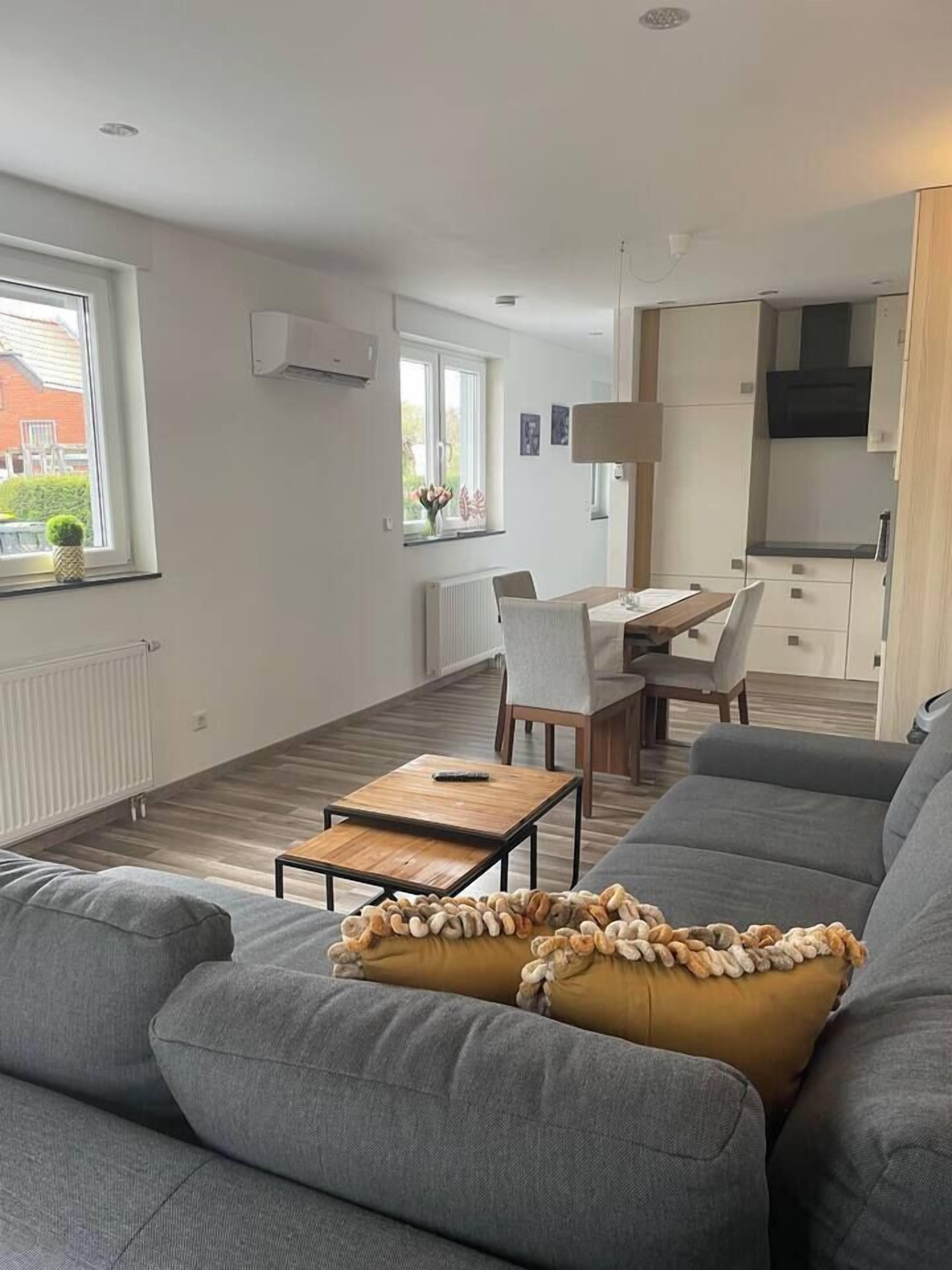 A modern living room with a grey sofa, a wooden coffee table, and a dining area with a table and chairs.