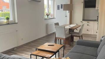 A modern living room with a grey sofa, a wooden coffee table, and a dining area with a table and chairs.