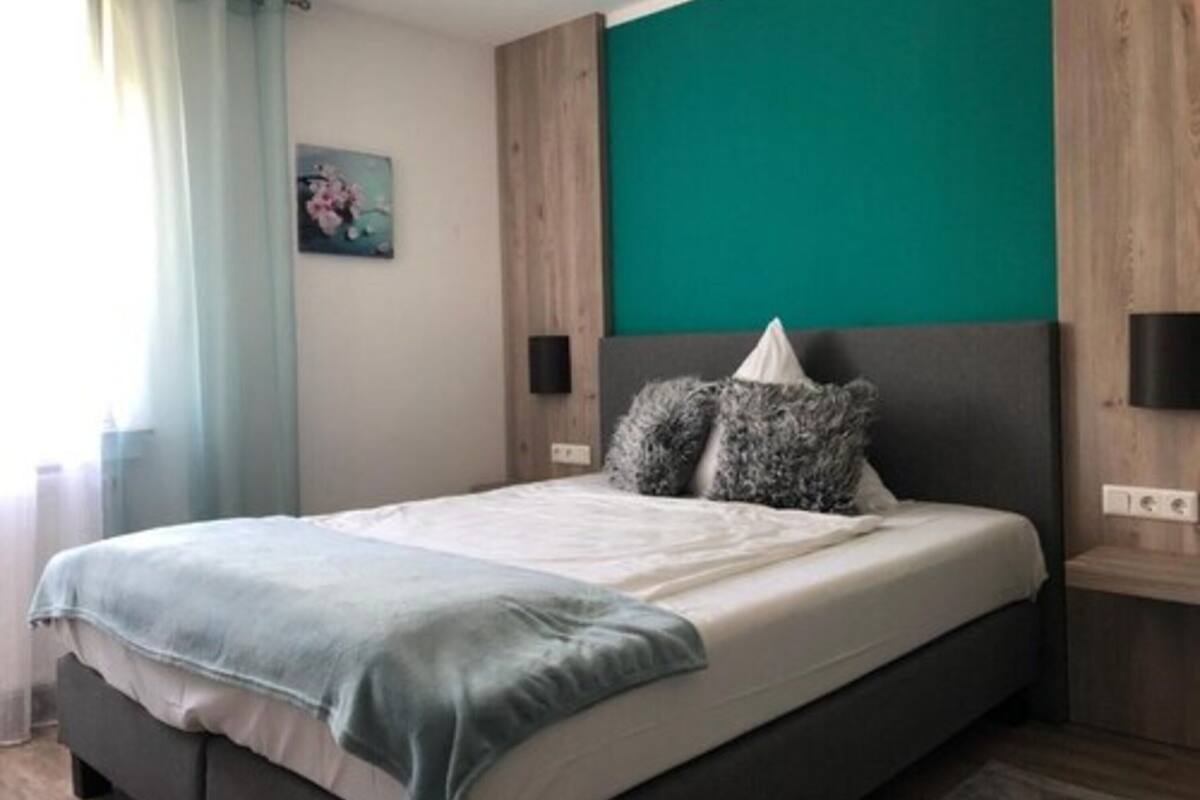 Een slaapkamer met een bed, een muur in teal, een houten hoofdeinde en een klein schilderij.