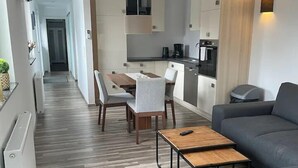 Un salon moderne avec un canapé gris, une table basse en bois et un coin repas comprenant une table et des chaises blanches.