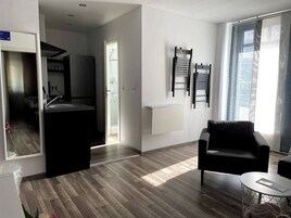 Uma sala de estar moderna com um sofá preto, uma mesa de centro redonda e uma janela grande com cortinas leves.