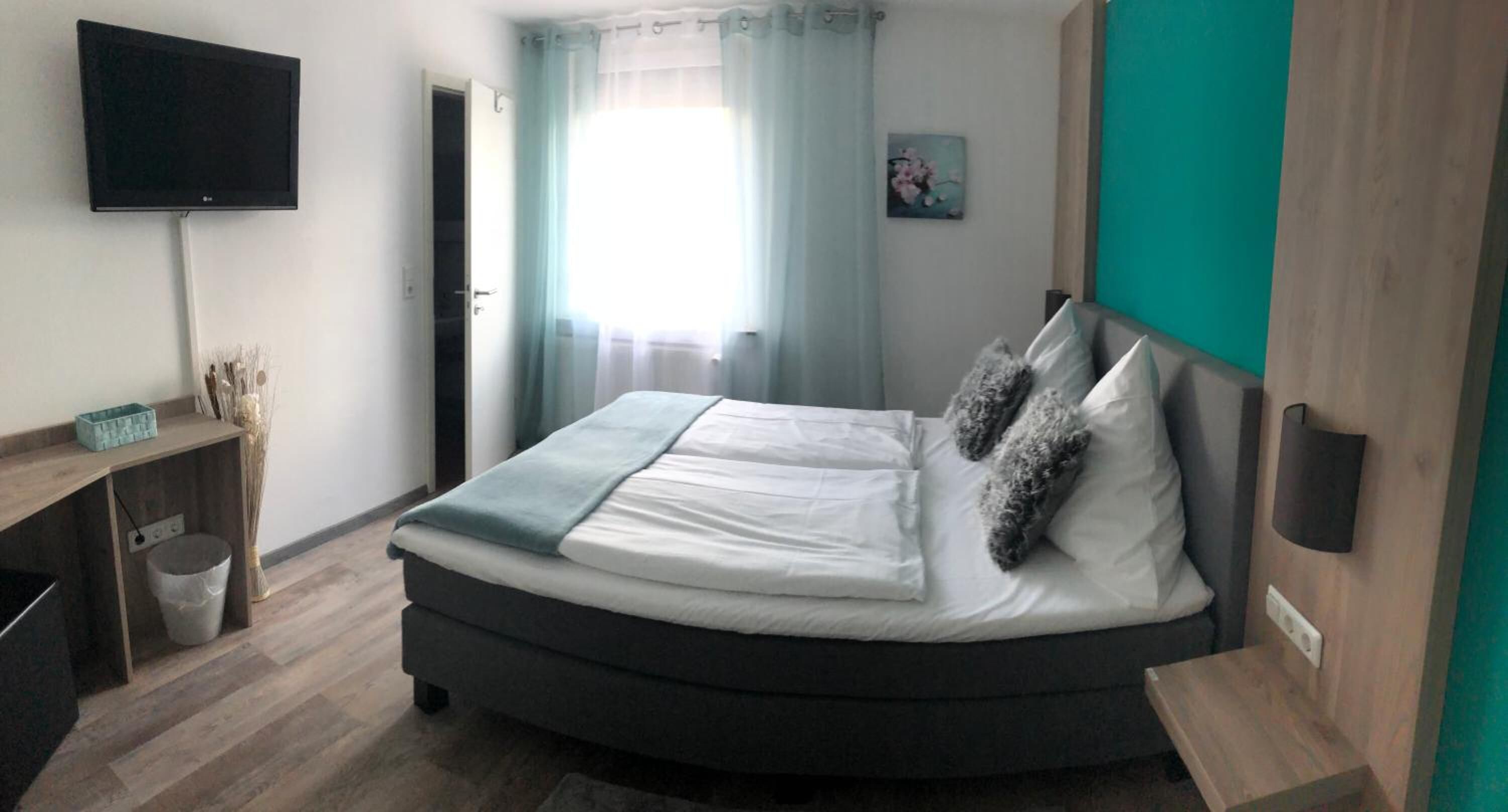 Un dormitorio con cama, escritorio, televisor y ventana con cortinas.