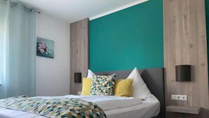Une chambre à coucher moderne avec un lit, une couvre-lit à motifs géométriques et un mur d’accent de couleur turquoise.