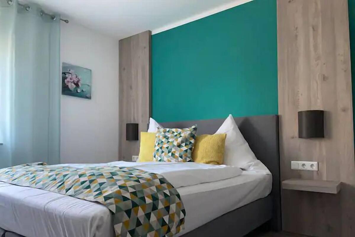 Een moderne slaapkamer met een bed, een bedovertrek met een geometrisch patroon en een wand in een teal kleur.