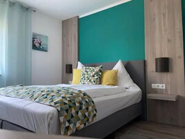 Quarto moderno com cama, colcha de padrão geométrico e parede de destaque azul-turquesa.