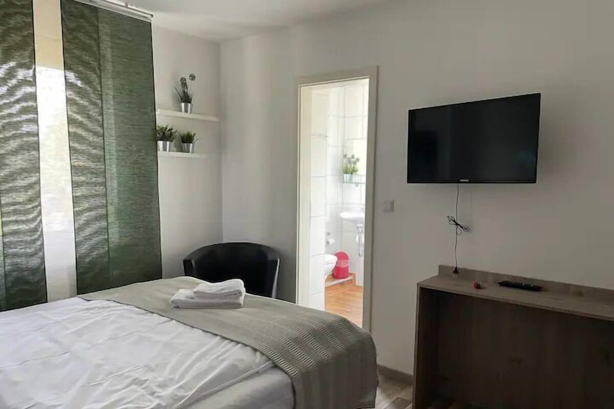 Een hotelkamer met een bed, een aan de muur bevestigde televisie, een stoel en een klein bureau met een afstandsbediening.