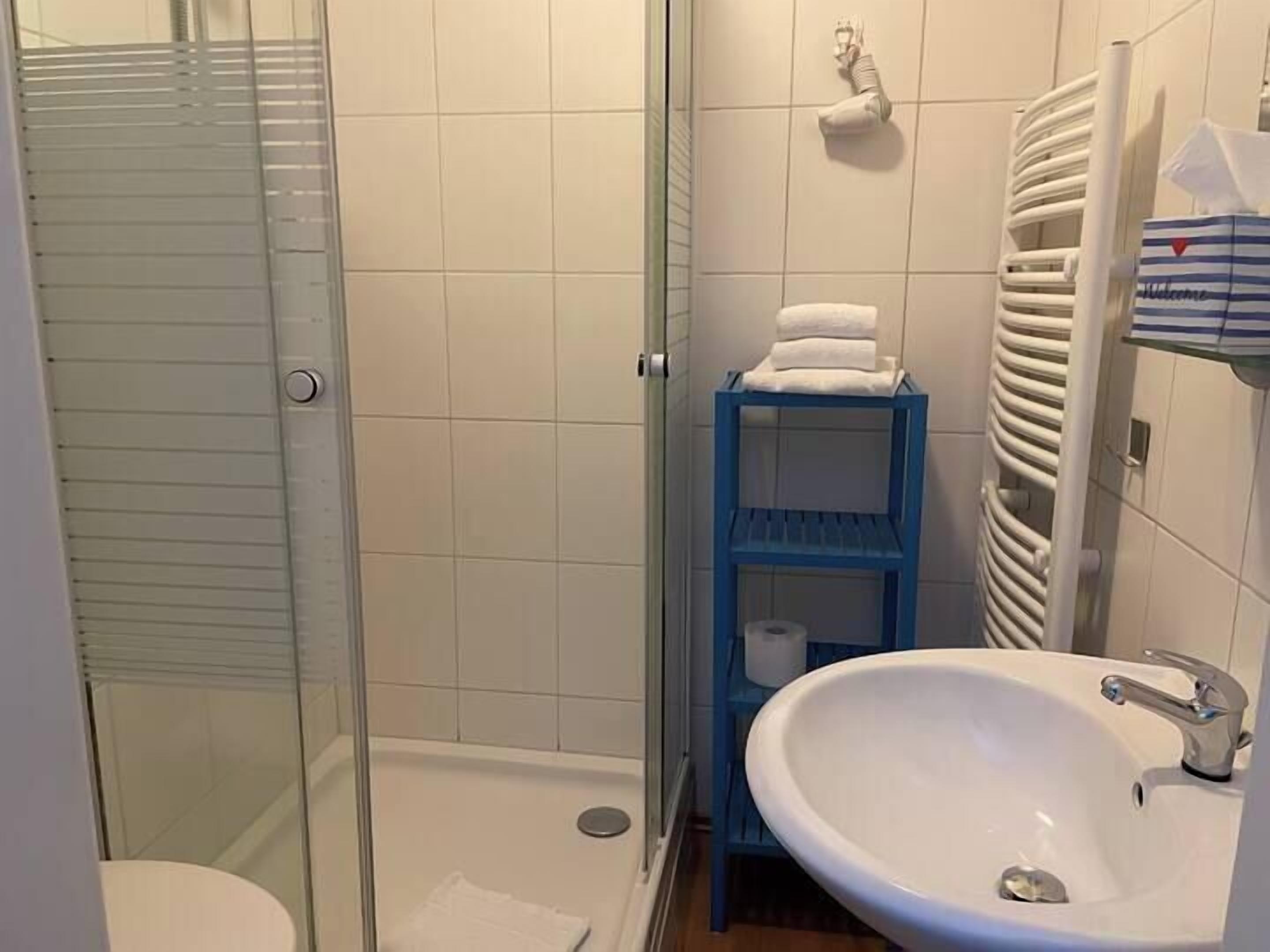 Ein Badezimmer mit Duschkabine aus Glas, einem weißen Waschbecken und einer blauen Regaleinrichtung.