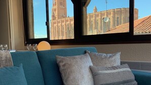 A teal sofa with cushions, a window with a view of a historic building, and a ceiling with exposed beams. - Cathedral Aparthotel historic center cathedral view Superior (Albi)