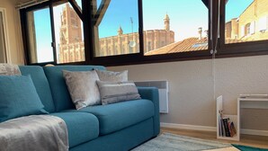 A modern living room with a teal sofa, a white radiator, and a view of a historic building through large windows. - Cathedral Aparthotel historic center cathedral view Superior (Albi)