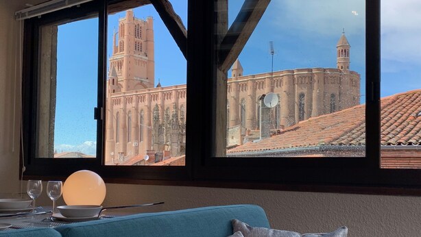 A room with a large window overlooking a historic building with a tall tower and arches. - Cathedral Aparthotel historic center cathedral view Superior (Albi)