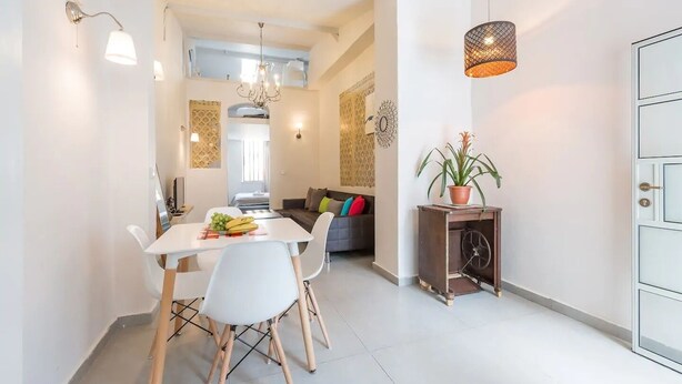 A modern kitchen with white cabinetry, a dining table with chairs, and a potted plant. - Home of Art in Neve-Tzedek Heart (Tel Aviv)