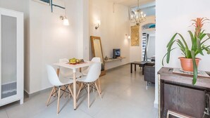 A modern dining area with a white table and chairs, a TV, and a potted plant. - Home of Art in Neve-Tzedek Heart (Tel Aviv)