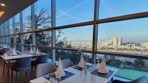 A restaurant with tables set for dining, large windows offering a city view, and modern interior design.