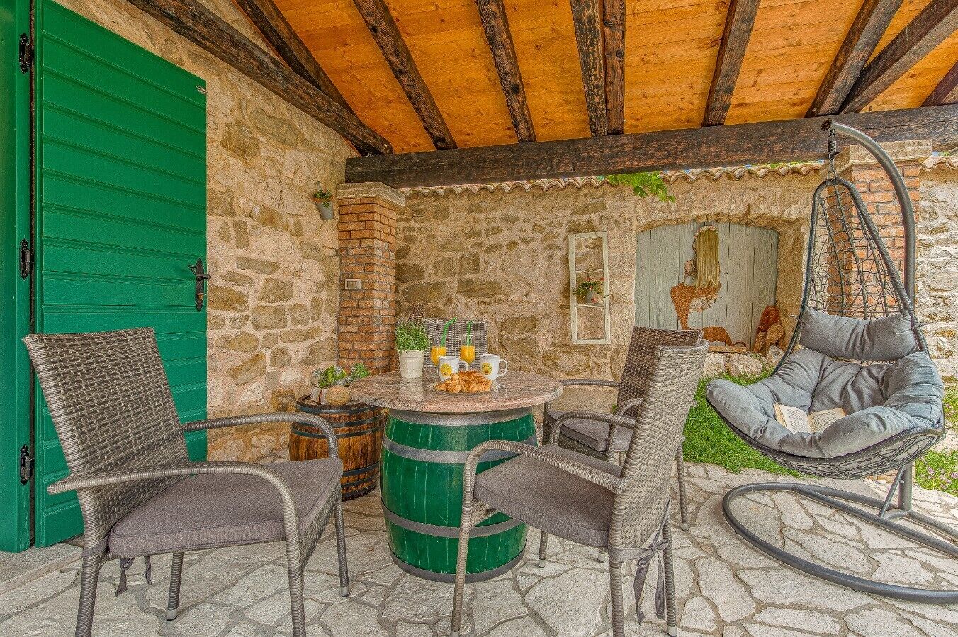 Un patio de piedra con mobiliario de mimbre, una silla colgante y una mesa dispuesta con comida y bebidas.