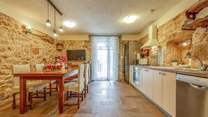 A kitchen with stone walls, wooden flooring, a dining table with chairs, and modern appliances. - Holiday Home Stone Wall (Razanac)