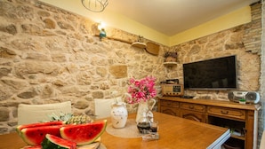 A stone-walled room with a wooden dining table, a television, and a radio. - Holiday Home Stone Wall (Razanac)